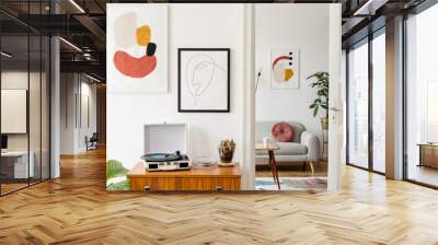 Stylish and retro living room with design  grey sofa, retro table, commode lamp and furniture. Mock up posters frames on the white walls. Minimalistic room with brown wooden parquet and plants. Wall mural