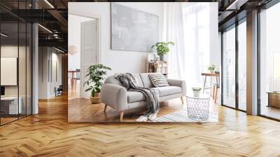 Stylish scandinavian living room with design furniture, plants, bamboo bookstand and wooden desk. Brown wooden parquet. Abstract painting on the white wall. Nice apartment. Modern decor of bright room Wall mural