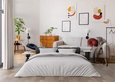 Stylish vintage decor in a spacious flat interior with design grey sofa, armchair, retro commode and posters on the wall. Brwon wooden parquet, stylish carpet and plants. Bright  living room. Wall mural