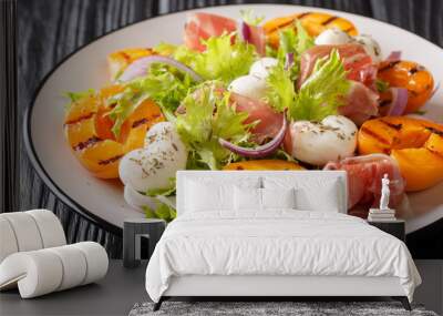 Delicious appetizer salad with mozzarella cheese, prosciutto, grilled apricots, red onion and fresh leafy lettuce close-up on the table. horizontal Wall mural