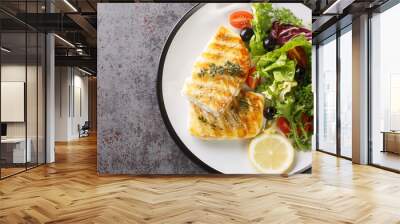 Delicious healthy grilled cod fish with fresh salad of tomatoes, olives, lettuce mix and lemon close-up in a plate on the table. Horizontal top view from above Wall mural