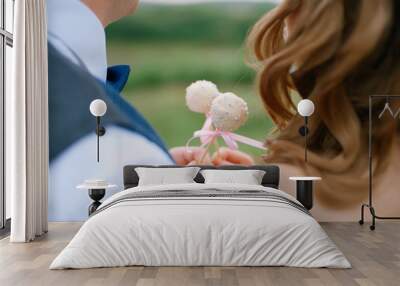 Hands of the groom in a blue suit and bow tie and the bride with cake Pops close-up, back Wall mural