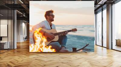 Portrait of happy smiling young man playing a guitar on a sea or ocean sand beach shore near the campfire bonfire. Evening sunset leisure, friends weekend enjoyment and relaxation, Wall mural