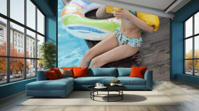 Closeup portrait of little girl inflates her swimming sleeves in the pool. Happy child having fun in water, beach resort, summer vacation and holidays concept. Girl showcasing a joyful summer vibe Wall mural