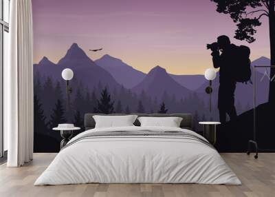 A tourist photographing a flying bird in a mountain landscape with forest under a morning sky with dawn and clouds Wall mural