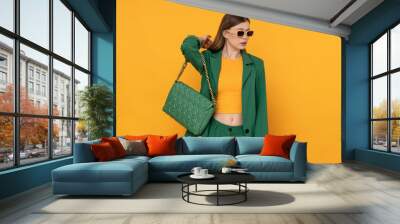 Fashionable female model in oversized green suit on isolated yellow background. Wall mural