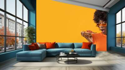 Happy African female with slice of pizza on isolated yellow background. Wall mural