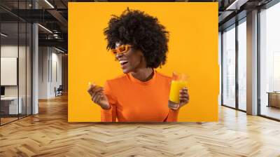 Happy woman is holding fresh orange juice on isolated orange background. Wall mural