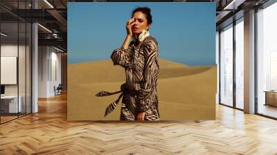 Model wearing animal print dress walking on sandy desert. Wall mural