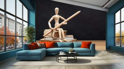 Wooden mannequin holding a pencil sitting on a pile of books. Back to school background Wall mural