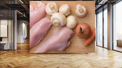 Fresh champignons, carrot, chicken fillet, and onion on wooden kitchen cutting board. Wall mural