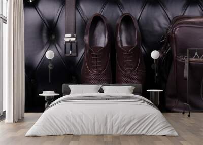 Men's fashion accessories wardrobe. Men's shoes, belt and bag against a black leather sofa. Wall mural