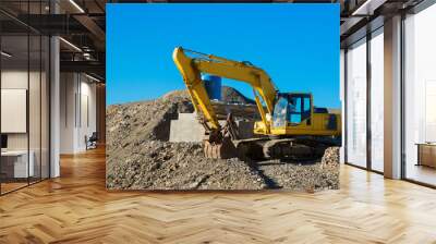 The excavator rakes in stones with his bucket. Excavator rakes rocky ground. Yellow excavator in work. Wall mural