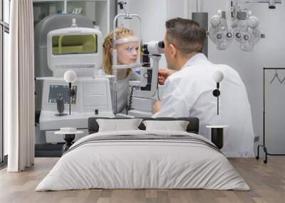 doctor and young patient in eye clinic, girl undergoing an eye test with professional optometrist using advanced diagnostic equipment, pediatric ophthalmology examination Wall mural