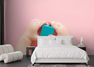 Baby girl hands holding and playing with light blue plastic shape on light pink table background. Pastel color. Closeup. Infant development toy. Point of view shot. Top down view. Wall mural