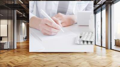 Doctor writing prescription for treatment of patient. Visit to physician at office. Medical and pharmacy concept. Different medicines on the table. Wall mural