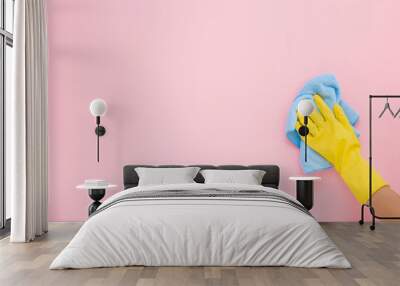 Employee hand in yellow rubber protective glove wiping pastel pink wall from dust with blue dry rag. General or regular cleanup. Commercial cleaning company. Copy space. Empty place for text or logo. Wall mural