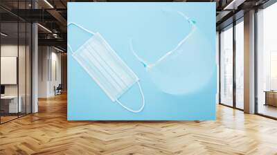 New transparent plastic visor with glasses and respirator mask for mouth and nose covering. Light blue table background. First protection in dangerous virus time. Healthcare concept. Top down view.  Wall mural