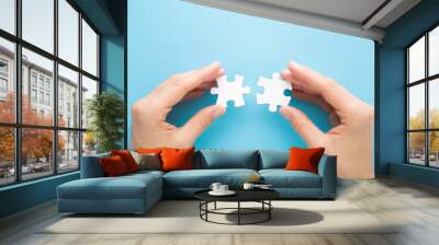 Young adult woman hand fingers holding and connecting different two white puzzle pieces on light blue table background. Pastel color. Closeup. Compatibility concept. Point of view shot. Top down view. Wall mural