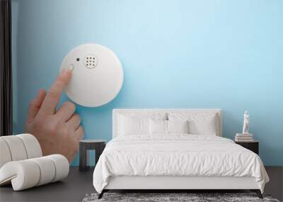 Young man finger touching new white plastic smoke alarm. Light blue table background. Pastel color. Safety concept. Empty place for text. Wall mural