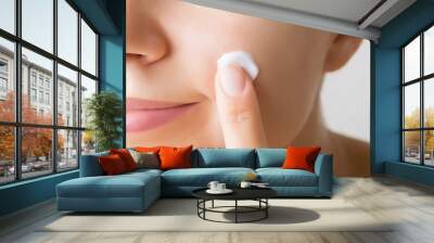 Young woman finger applying white moisturizing cream on cheek. Care about clean and soft face skin. Daily beauty product. Closeup. Wall mural