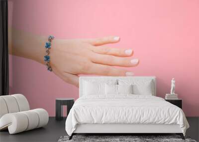 Young woman hand with blue flower bracelet on wrist. Isolated on pink background. Pastel color. Care about hand skin and nails. Closeup. Wall mural