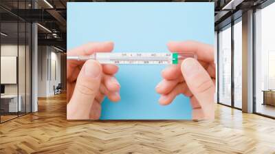 Young woman hands holding mercury thermometer on pastel blue background. Fever and healthcare concept. Closeup. Point of view shot. Top down view. Wall mural