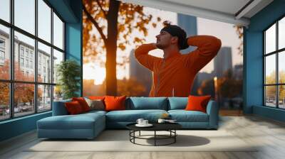 A man relaxes outdoors in an orange jacket during sunset in an urban park surrounded by fall foliage Wall mural