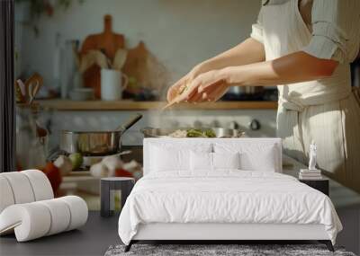 A person prepares a fresh pasta dish with vegetables in a cozy kitchen filled with natural light and herbs Wall mural