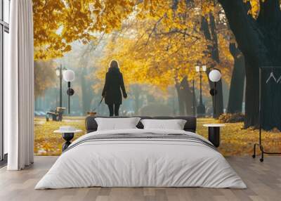 A woman walks her dog through an autumn park filled with golden leaves on a crisp afternoon Wall mural