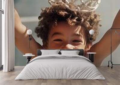 A young boy joyfully hanging from a basketball hoop in an outdoor court during a sunny day, showcasing his playful spirit and excitement Wall mural