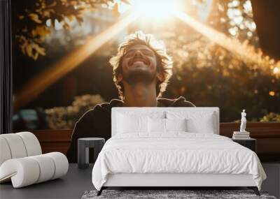 A young man enjoys sunlight while sitting on a park bench in the late afternoon Wall mural