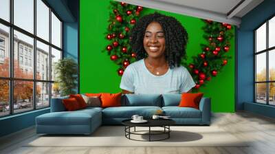 African woman smiling standing against Christmas wreath decor at home Wall mural