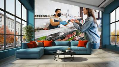 Butcher's shop seller helps to choose product to woman customer Wall mural