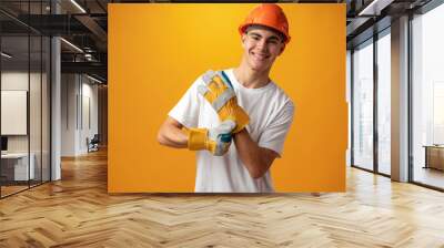 Confident smiling teen boy wearing orange hard hat against yellow background Wall mural