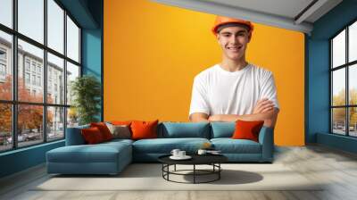 Confident smiling teen boy wearing orange hard hat against yellow background Wall mural