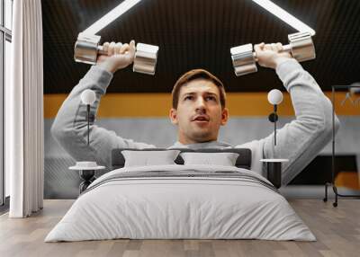 Determined handsome young male working out in gym with dumbbells Wall mural