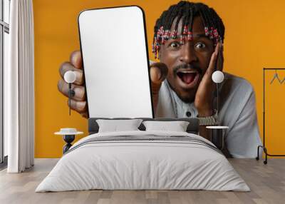 Excited young african man holding smartphone with white blank screen in hand on yellow studio background Wall mural