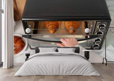 Female hand taking delicious croissants out of electric oven in kitchen Wall mural