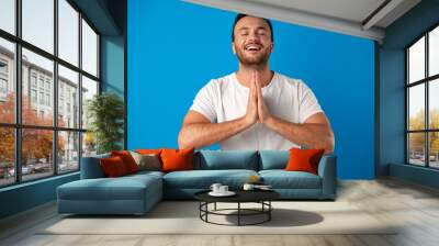 Focused handsome young man meditating on camera over blue background Wall mural