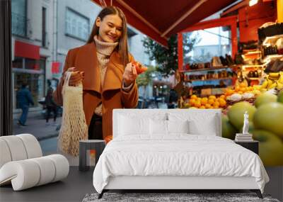 Good looking young woman standing in front of fruit shelves buying groceries in the street Wall mural