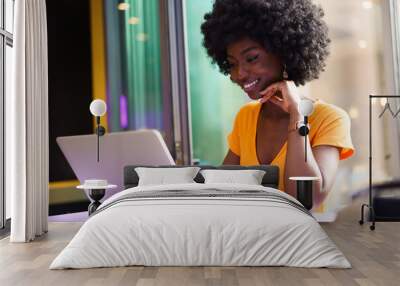 Happy beautiful young black woman using laptop in cafe Wall mural