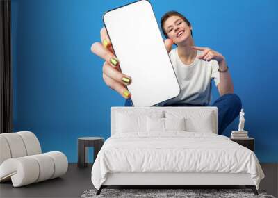 Happy woman shows blank smartphone screen against blue background Wall mural