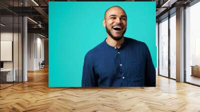 Joyful dark-skinned man laughing against turquoise background Wall mural