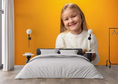 Little beautiful smiling girl holding book against yellow background Wall mural