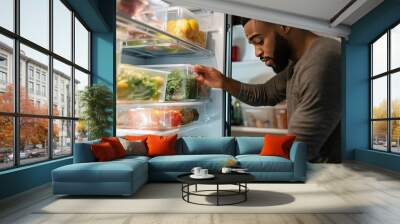 Man organizing fresh vegetables and fruits in a refrigerator at home during a weekend meal prep session for healthy eating Wall mural