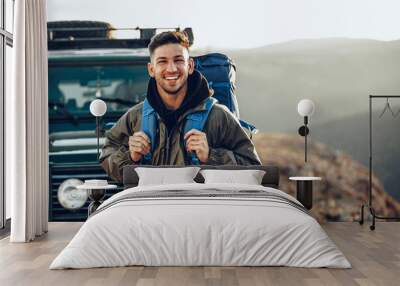 Portrait of a young traveler man in hiking equipment standing near his off-road car Wall mural