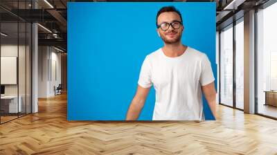 Portrait of smiling handsome guy in white t-shirt over blue background Wall mural