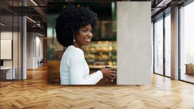 Portrait of young african woman with afro hairstyle smiling in urban background Wall mural