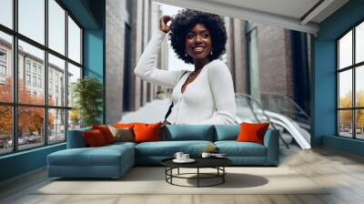 Portrait of young african woman with afro hairstyle smiling in urban background Wall mural